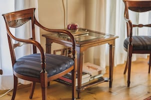 Una silla de madera con asiento y respaldo acolchados, ubicada frente a una mesa de vidrio con un libro y un jarrón rojo encima.