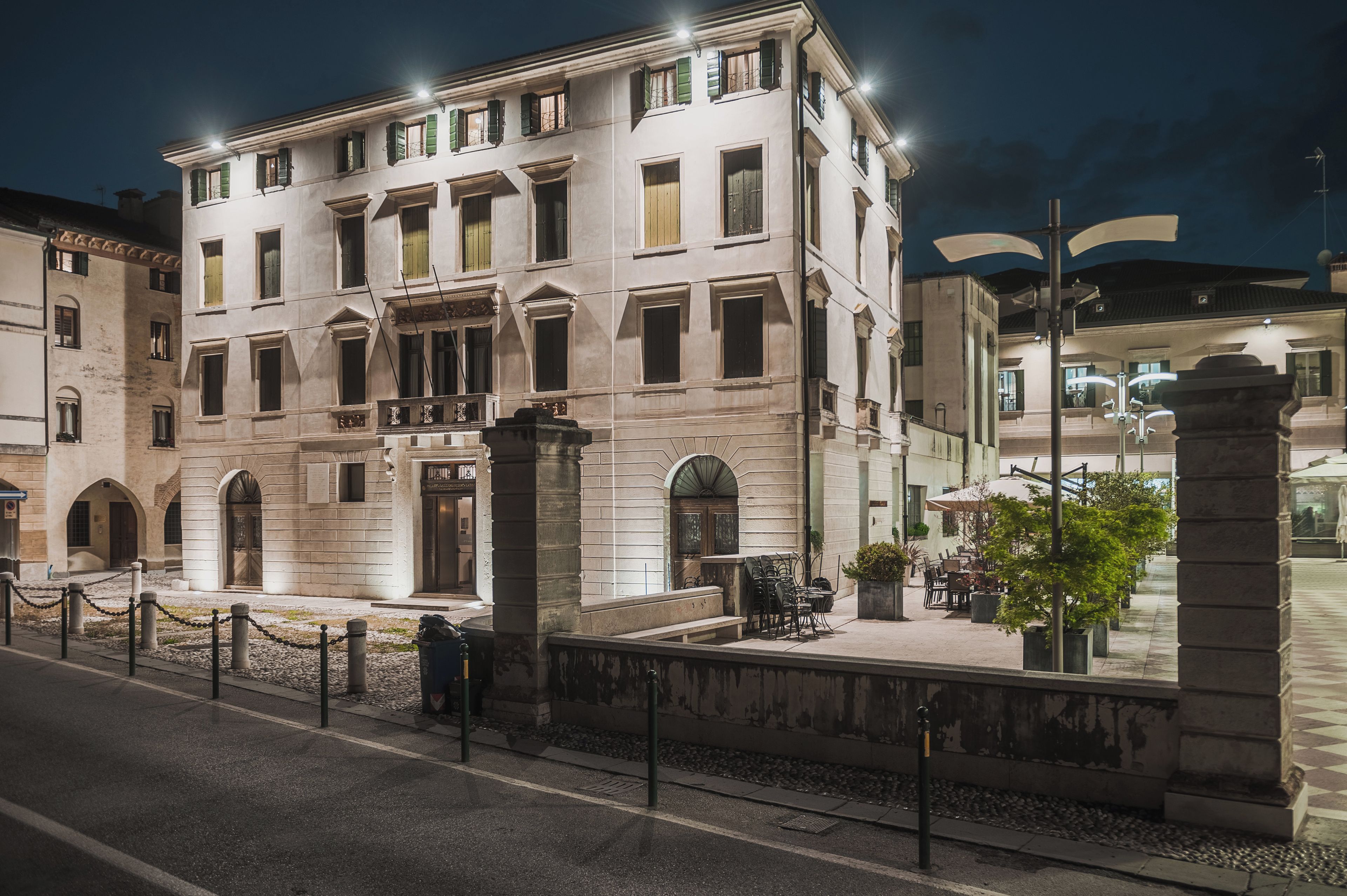 Un edificio histórico con entrada central, varias ventanas y un patio con mesas al aire libre.