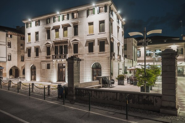 Un edificio histórico con entrada central, varias ventanas y un patio con mesas al aire libre.