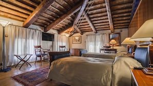 Una camera accogliente con travi in legno, un letto grande, due poltrone, una scrivania e una lampada.