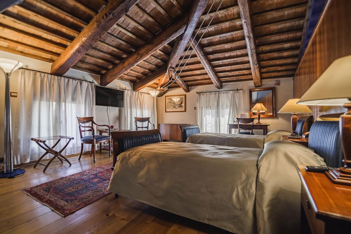 Ein gemütliches Schlafzimmer mit Holzbalken, einem großen Bett, zwei Sesseln, einem Schreibtisch und einer Lampe.