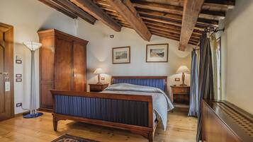 Une chambre à coucher avec un lit en bois, une armoire, deux tables de chevet avec des lampes, un radiateur et une fenêtre avec des rideaux.