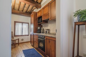 Une cuisine avec des meubles de rangement en bois, un four encastré et une fenêtre avec des rideaux.