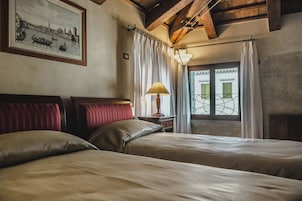 Una habitación de hotel con dos camas, un cuadro enmarco con vista a la ciudad, una ventana con cortinas y una lámpara.