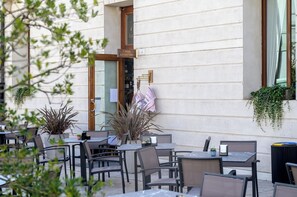 Un café al aire libre con mesas y sillas, un letrero que dice 'CAFFÈ LETTERARO' y plantas en macetas.