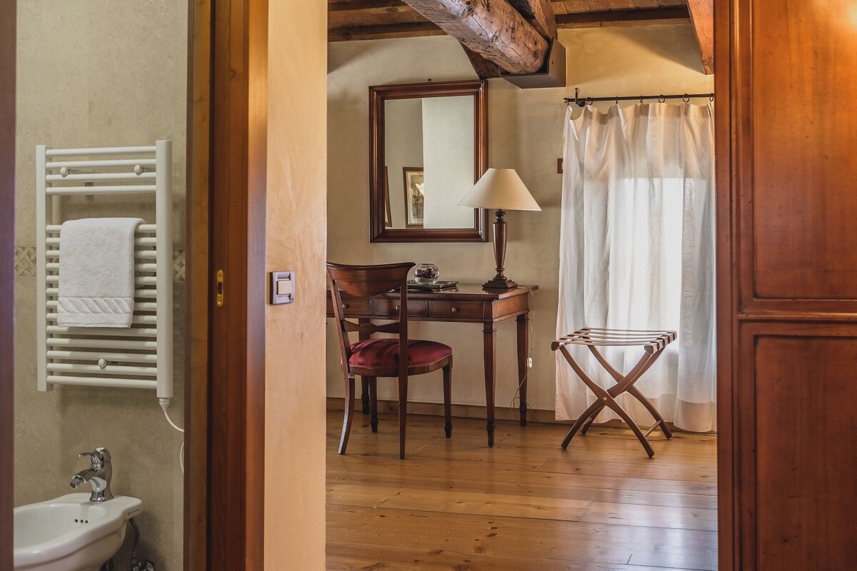 Un plancher en bois, une chaise en bois, un bureau avec une lampe, un miroir, un porte-serviettes et un rideau de douche.