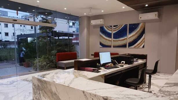 Un mostrador de recepción moderno con encimera de mármol, una computadora portátil y un monitor. Se observa un muro de vidrio con vistas a edificios.