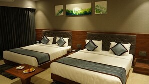 A hotel room with two beds, a wooden headboard, a small table with a plate of fruit, and abstract wall art. - Alaukik Hotel (Rahata)
