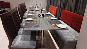 A dining area with a long table, chairs, and a sofa. - Alaukik Hotel (Rahata)