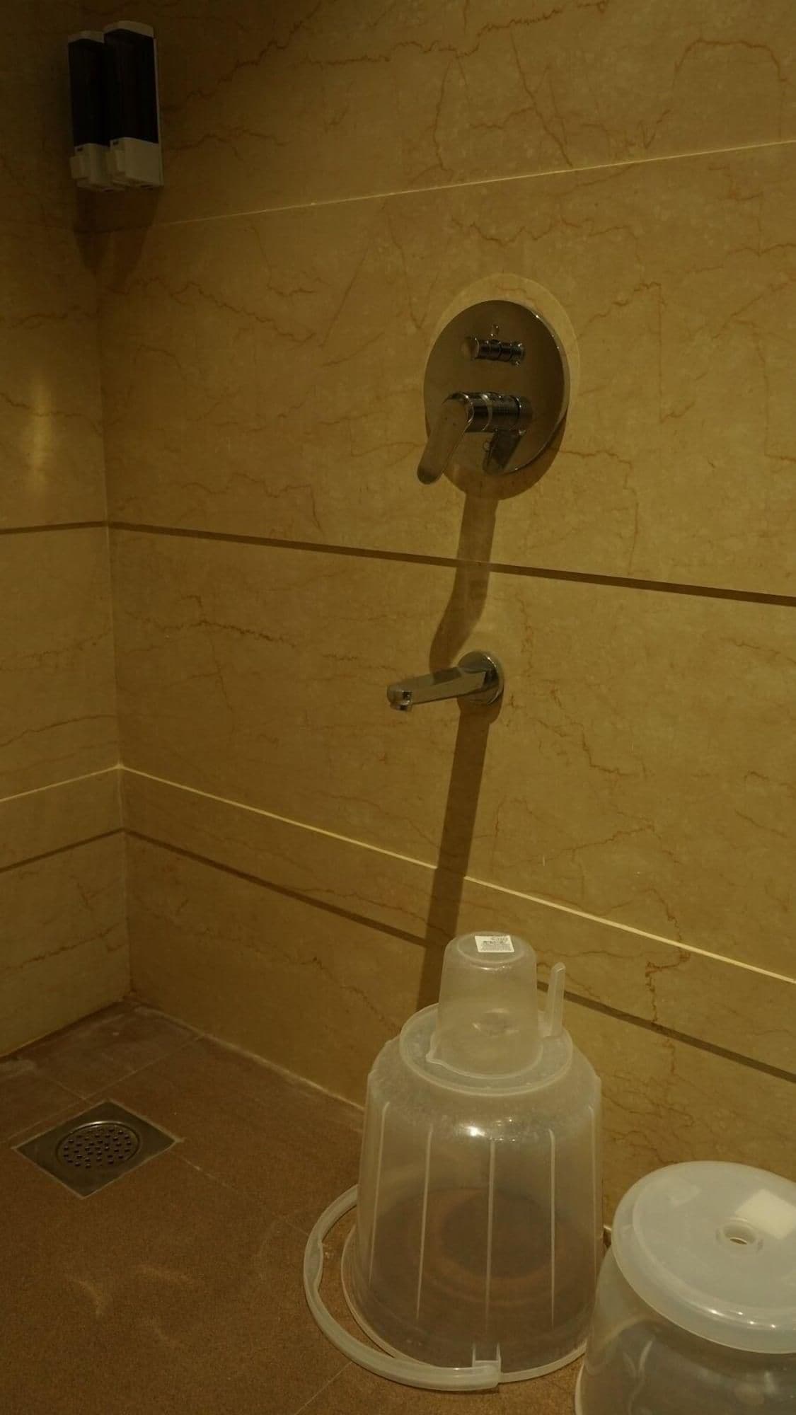 Un baño con pared de mármol, ducha, inodoro y cubo de basura.