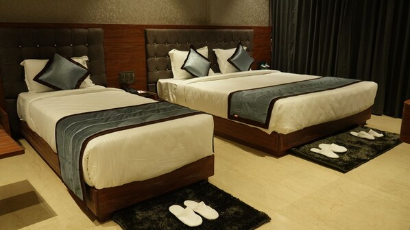 A hotel room with two beds, each with a wooden headboard and white bedding. There are slippers on a black rug in front of each bed. - Alaukik Hotel (Rahata)