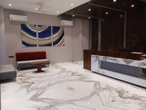 A modern reception area with a marble floor, a red sofa, and a large abstract painting on the wall.