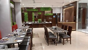Un restaurante con varias mesas, sillas y una zona de recepción con mostrador de madera.