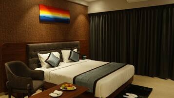 A hotel room with a bed, a chair, a table with a fruit plate, and a painting on the wall.