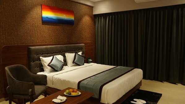 A hotel room with a bed, a chair, a table with a fruit plate, and a painting on the wall. - Alaukik Hotel (Rahata)