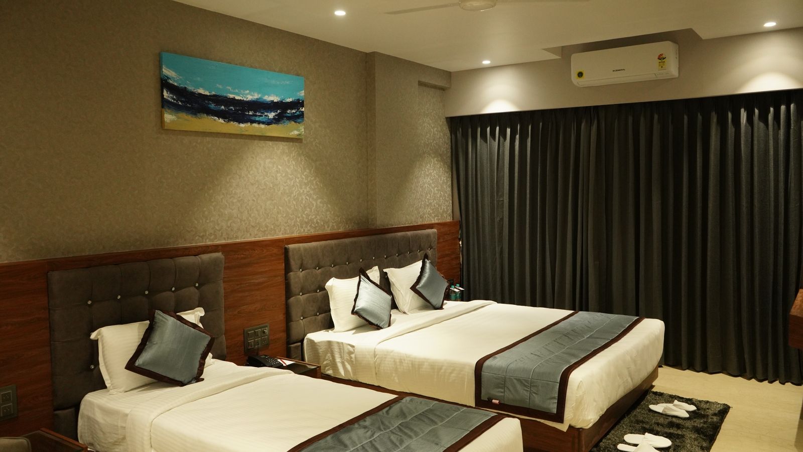 Habitación de hotel con dos camas, un cuadro, una ventana con cortinas y un equipo de aire acondicionado.