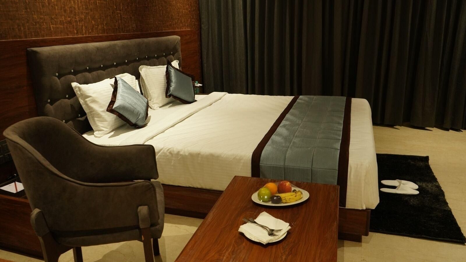 Una habitación de hotel con una cama, una silla, una mesa con fruta y una servilleta, y una alfombra negra.