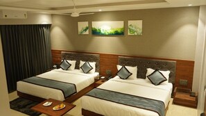 A hotel room with two beds, a small table with a plate of fruit, and artwork on the wall. - Alaukik Hotel (Rahata)