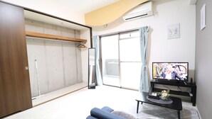 Una sala de estar moderna con un sofá azul, un televisor sobre un mueble bajo y un ventanal corredizo que da a un balcón.