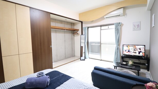 Una habitación de hotel con cama, sofá, televisión y puerta corredera que da a un balcón.