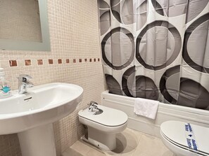 Ein Badezimmer mit Waschbecken, Toilette und Bidet. Die Wände sind mit einem gemusterten Fliesenbelag versehen.