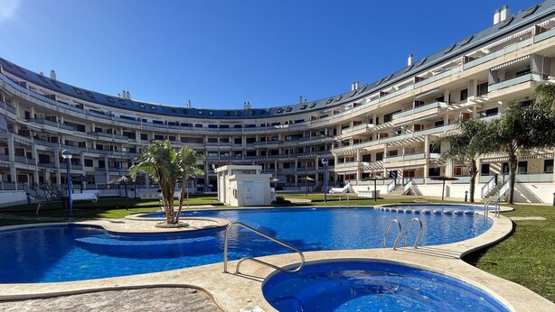 Un hotel de varios niveles con piscina central, zona de estar al aire libre y césped cuidado.