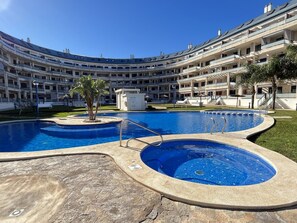 Ein mehrstöckiges Hotel mit einem zentral gelegenen Schwimmbad, Außenbereich zum Sitzen und einem gepflegten Rasen.