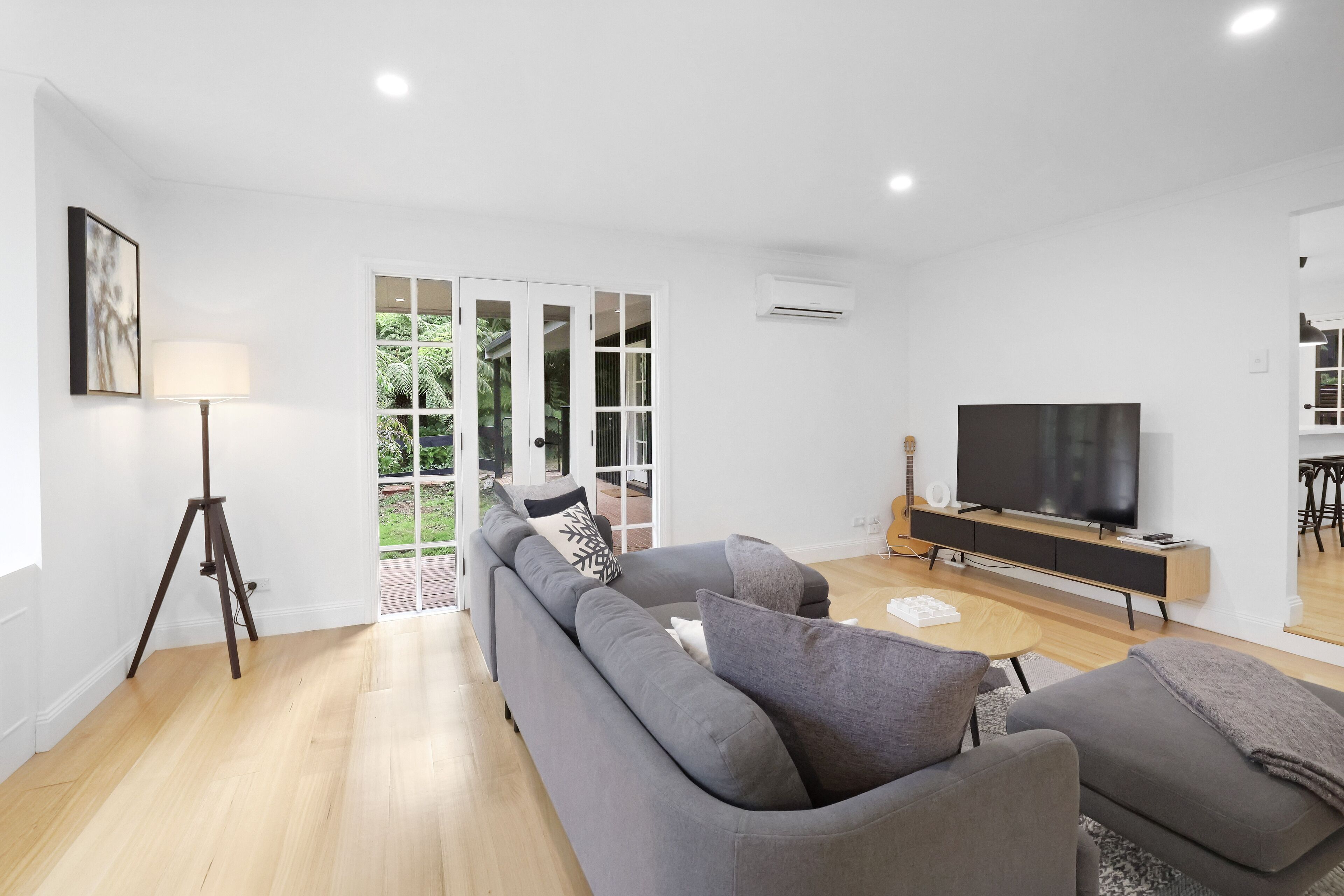 Un salon moderne avec un canapé gris, un téléviseur posé sur un meuble en bois et une lampe sur pied.