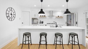 Een moderne keuken met een centraal eiland, zwarte hanglampen en een grote wandklok.