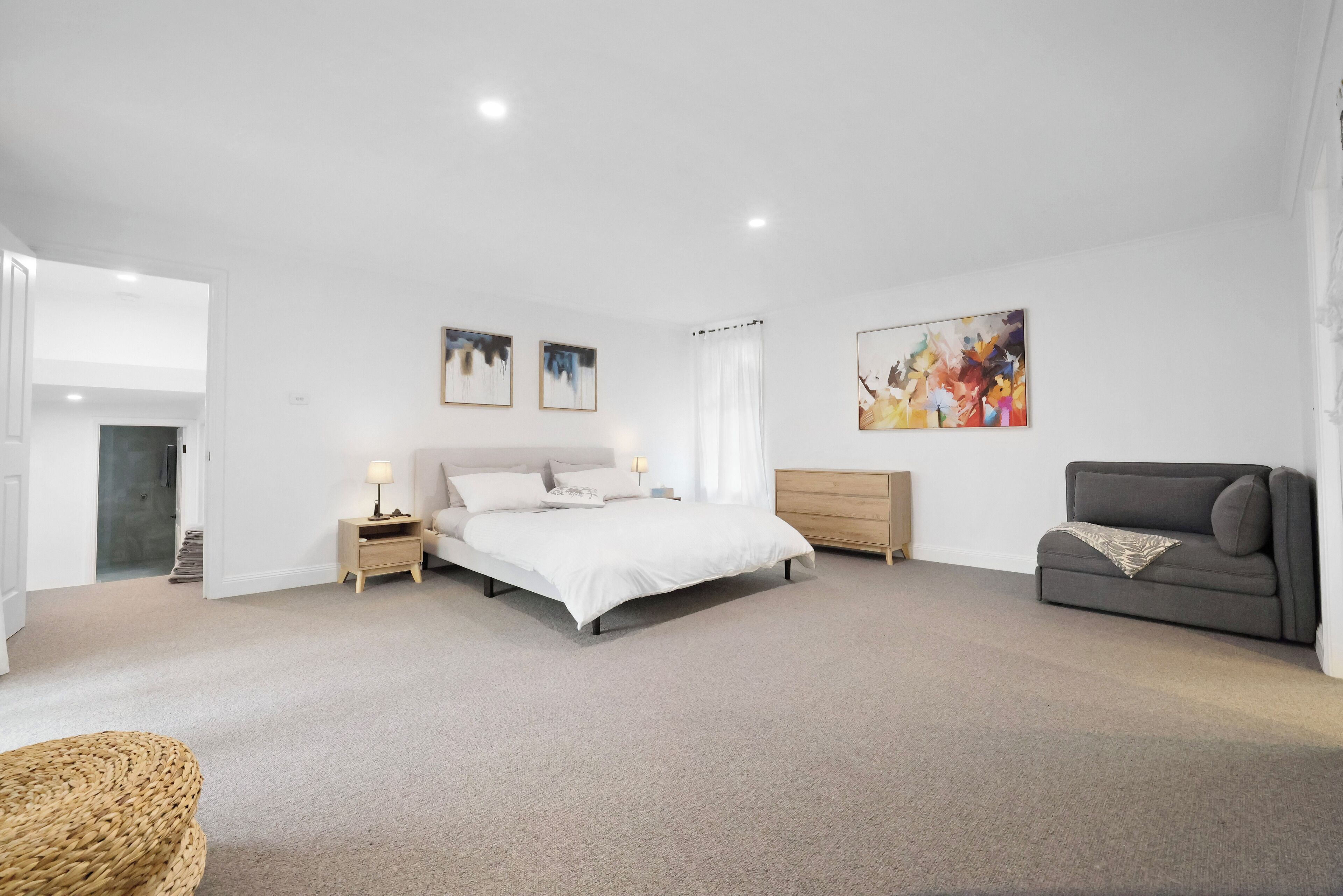 A spacious bedroom with a large bed, a gray sofa, and a wooden nightstand.