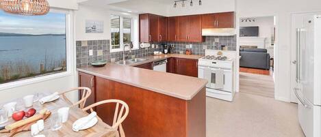 A modern kitchen with a central island, wooden cabinets, and a view of the water.