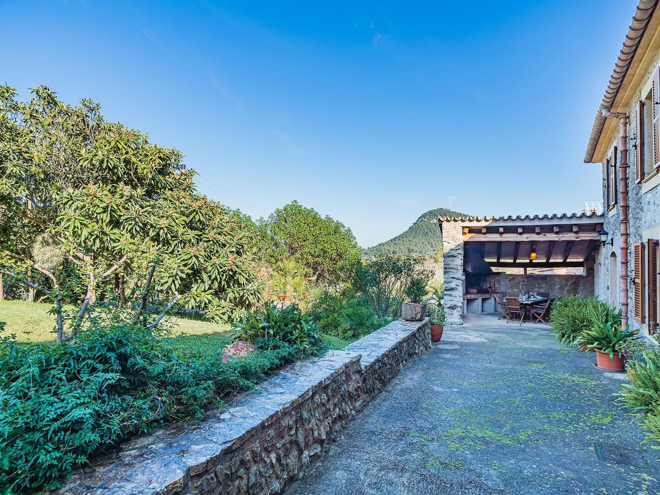 A courtyard with a stone wall, a pergola, and a dining area with outdoor furniture.