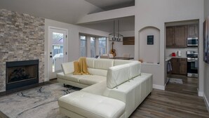 A modern living room with a sectional sofa, a fireplace, and a kitchen area visible through an open door. - Gourmet Kitchen with Large Dining Table, Quiet Neighborhood, Close to COTA and Airport (Austin)