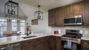 A modern kitchen with dark wooden cabinets, stainless steel appliances, a marble countertop, and pendant lighting. - Gourmet Kitchen with Large Dining Table, Quiet Neighborhood, Close to COTA and Airport (Austin)
