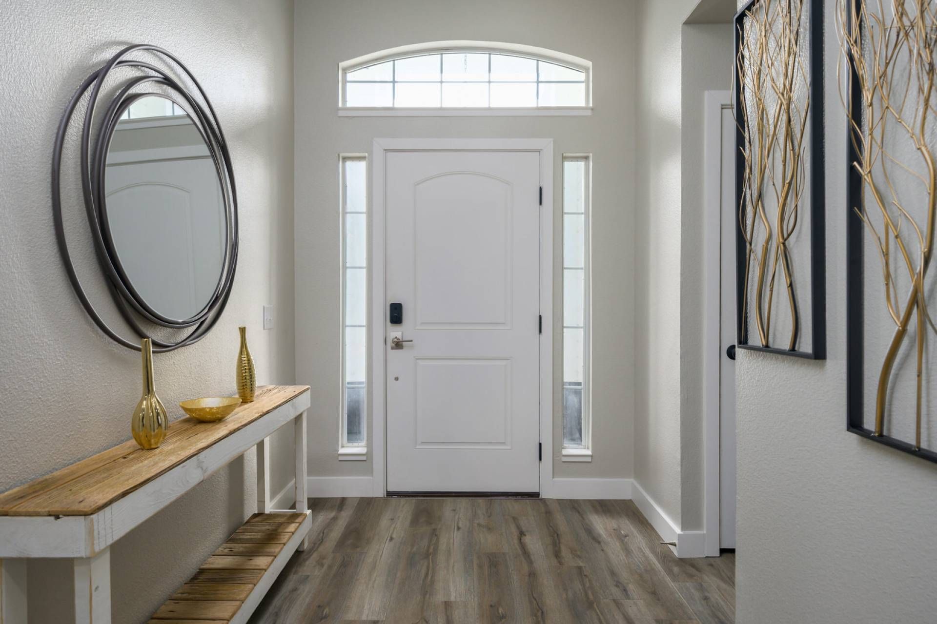 A hallway with a white door, a wooden bench with a vase, and a wall-mounted mirror.