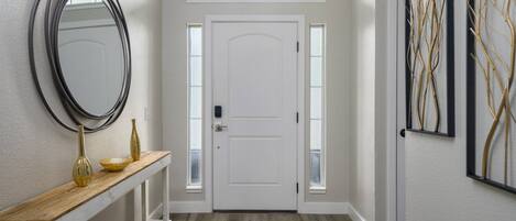 A hallway with a white door, a wooden bench with a vase, and a wall-mounted mirror.