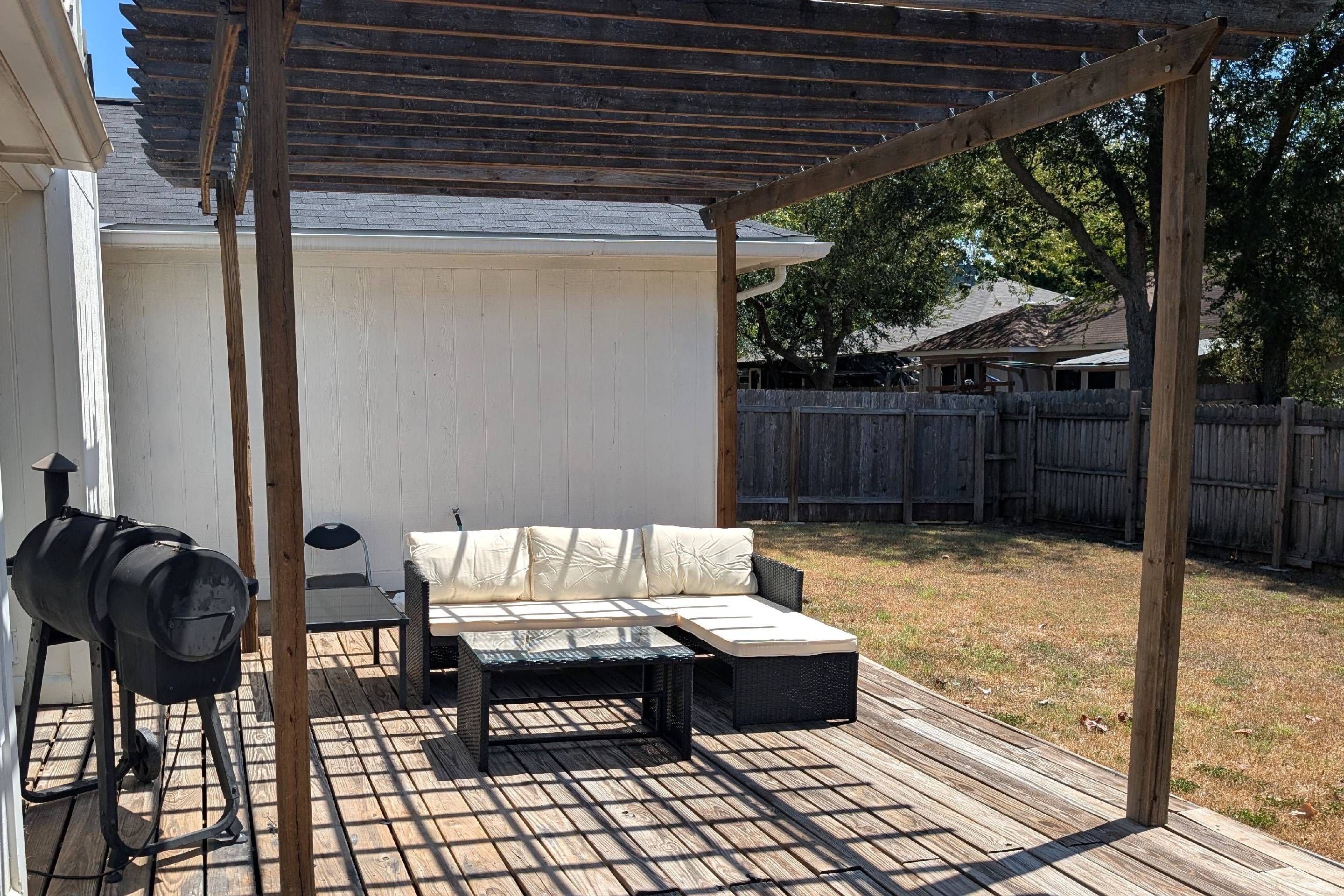 A covered outdoor patio with a grill, a cushioned seating area, and a wooden deck.