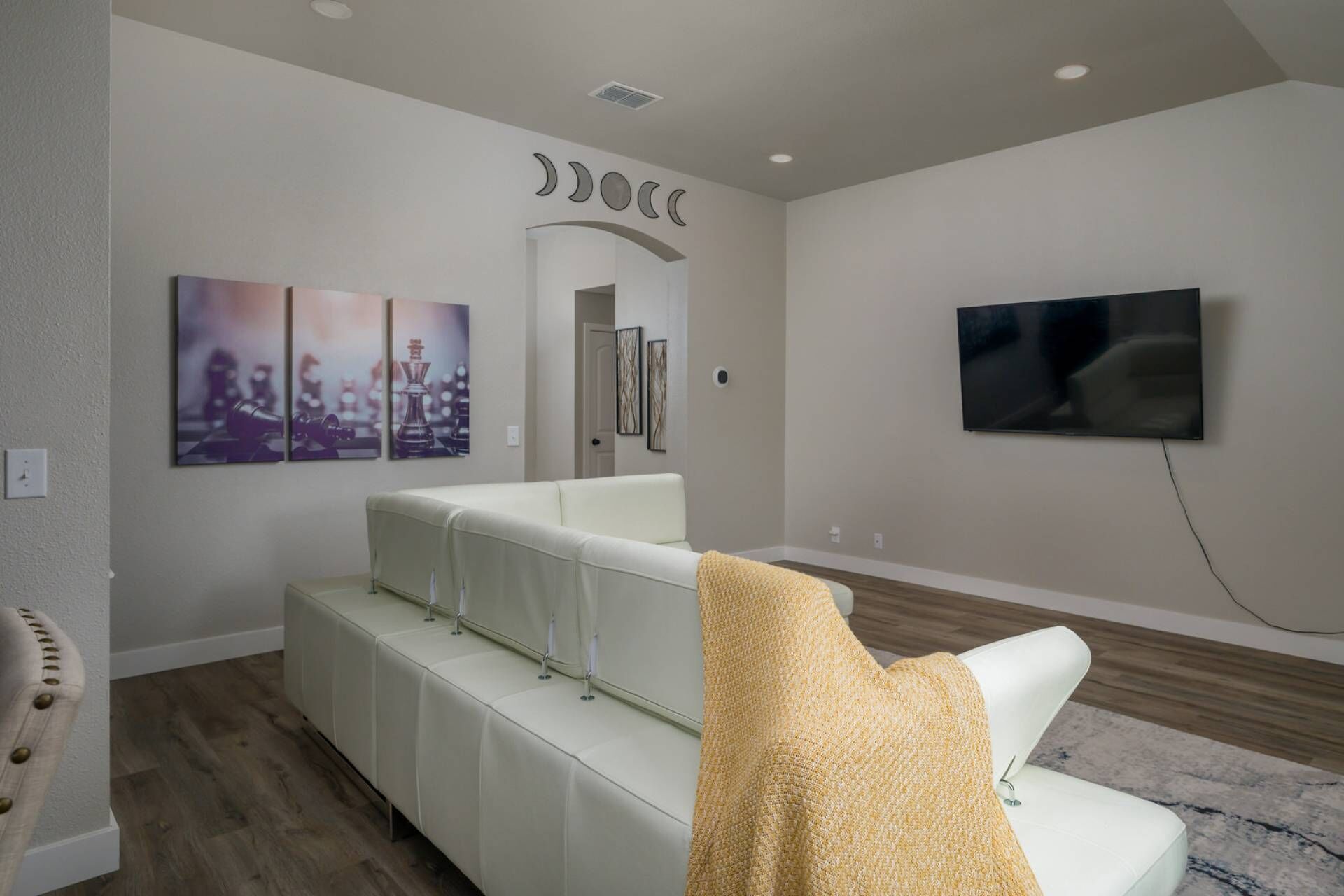 Una sala de estar moderna con un sofá blanco, un televisor montado en la pared y obras de arte decorando la pared.