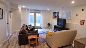 A living room with a sofa, a coffee table, a TV, and a plant. - Cozy Home Away from Home (Kingston)