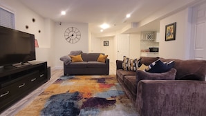 A living room with a flat-screen TV, a sofa, a loveseat, and a patterned rug. - Cozy Home Away from Home (Kingston)