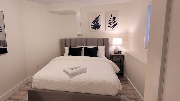 A bedroom with a bed, a nightstand, a lamp, and two framed leaf decorations on the wall. - Cozy Home Away from Home (Kingston)