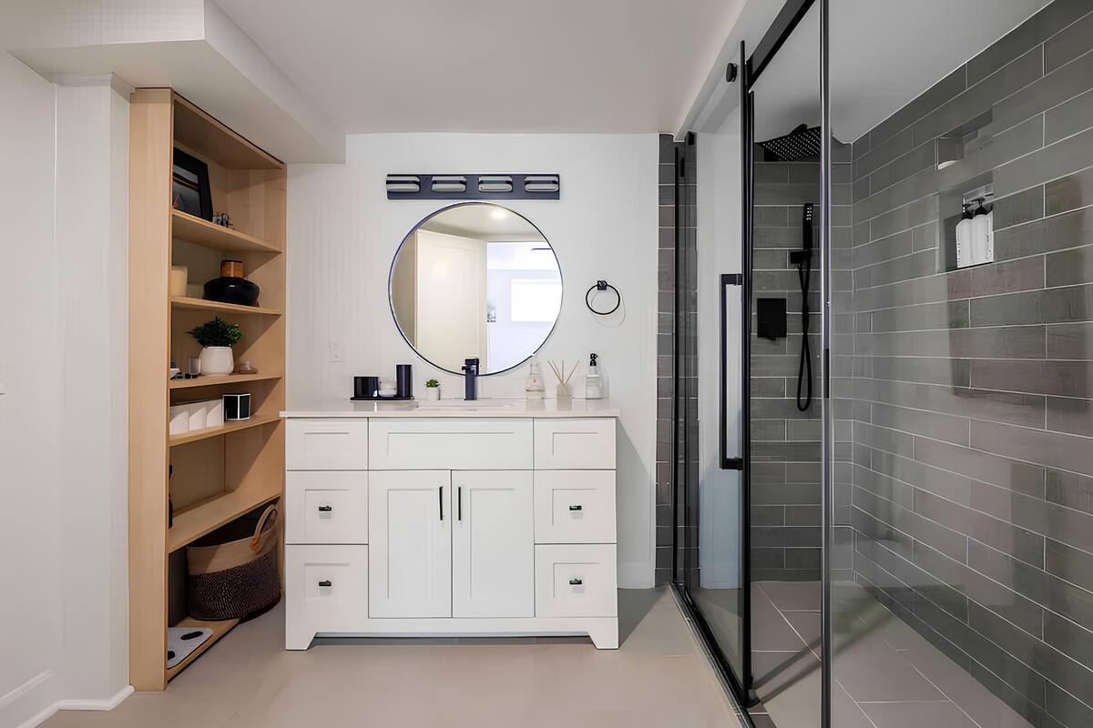 Une salle de bain moderne avec un meuble-lavabo blanc, un miroir rond et une cabine de douche en verre.
