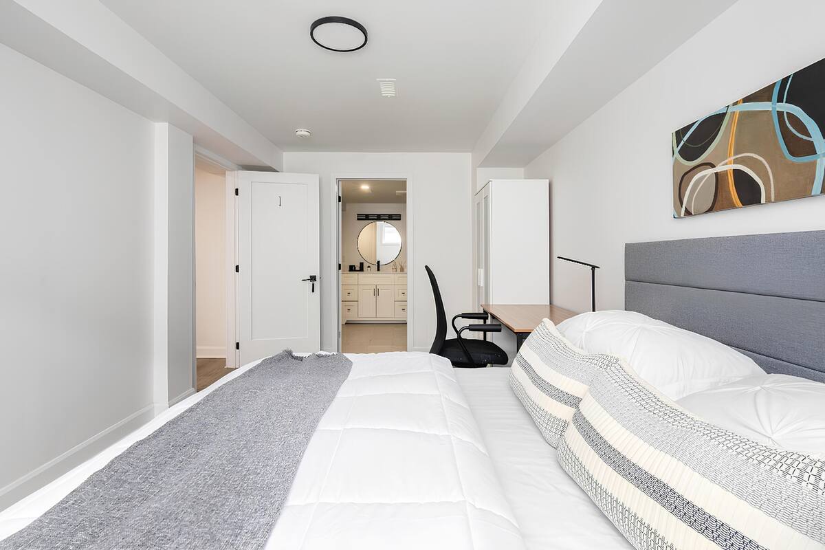 Une chambre moderne avec un grand lit, un bureau et une chaise. On peut apercevoir la salle de bain à travers une porte ouverte.