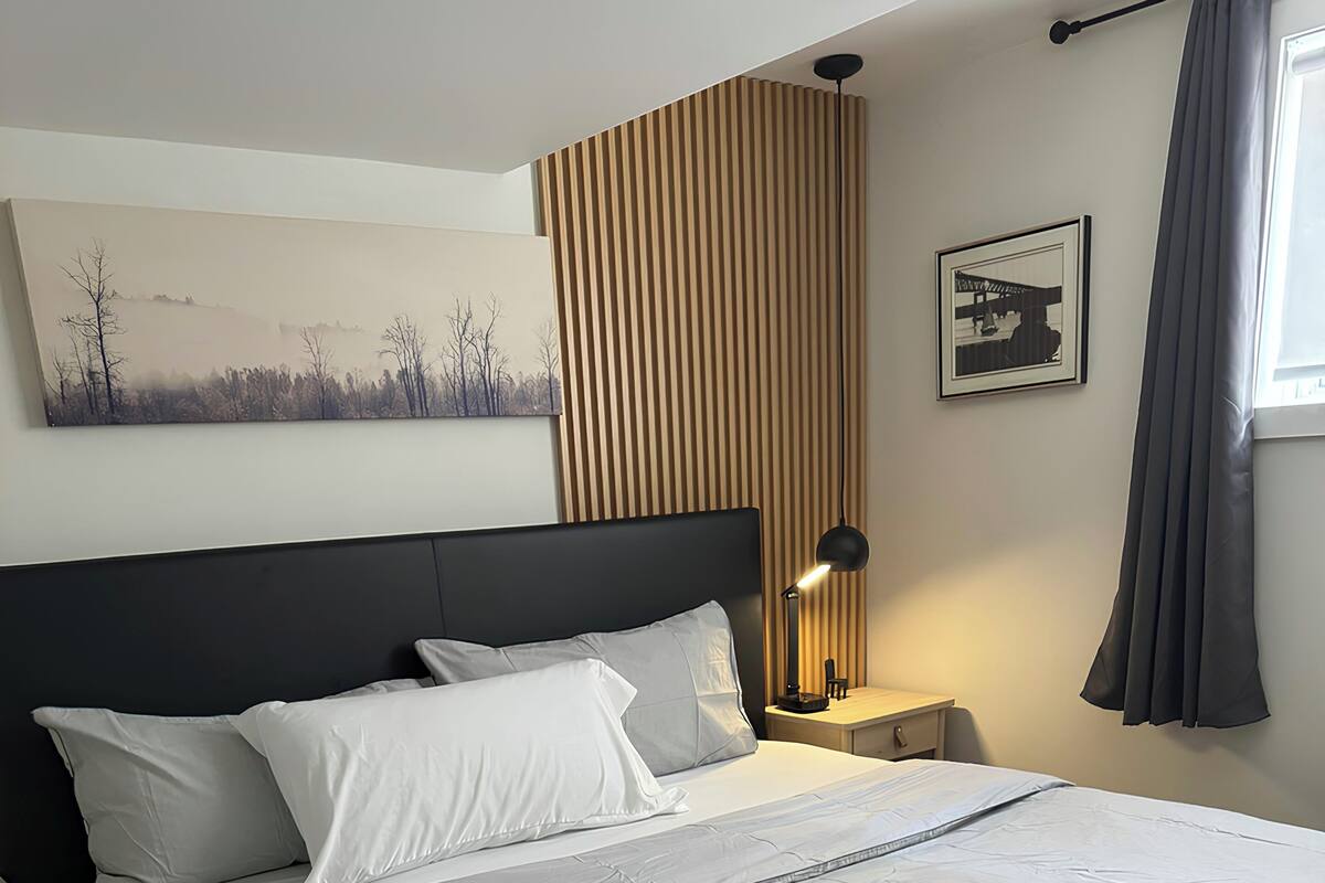 Un lit bien fait, avec du linge de lit blanc, une tête de lit sombre et une lampe de chevet.