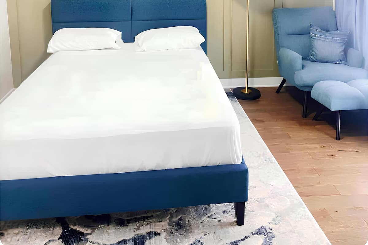 Une chambre à coucher comprenant un lit, une chaise, une lampe sur pied et un élément d écoratif mural.