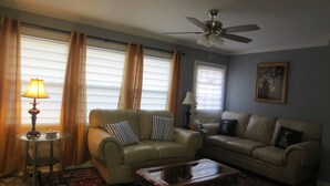 Ein Wohnzimmer mit zwei Ledersofas, einem Glastisch, einem Deckenventilator und einem gemusterten Teppich.