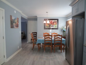 Uma sala de jantar com mesa, cadeiras, geladeira e obras de arte nas paredes.