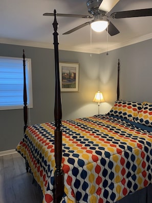 Quarto com cama de dossel, ventoinha no teto, quadro na parede e janela com persianas.