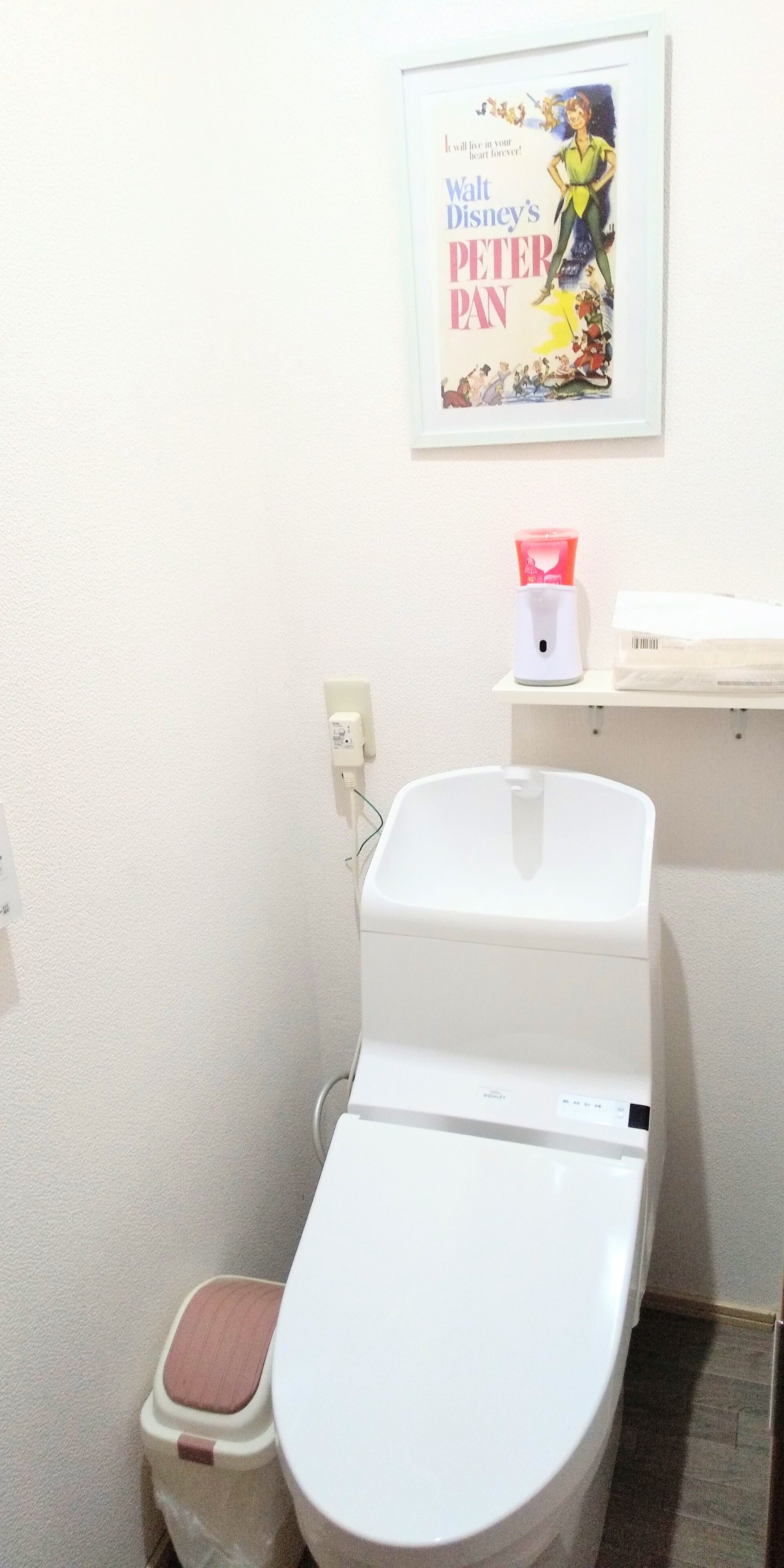 A bathroom with a toilet, a bidet, a soap dispenser, and a framed poster on the wall.