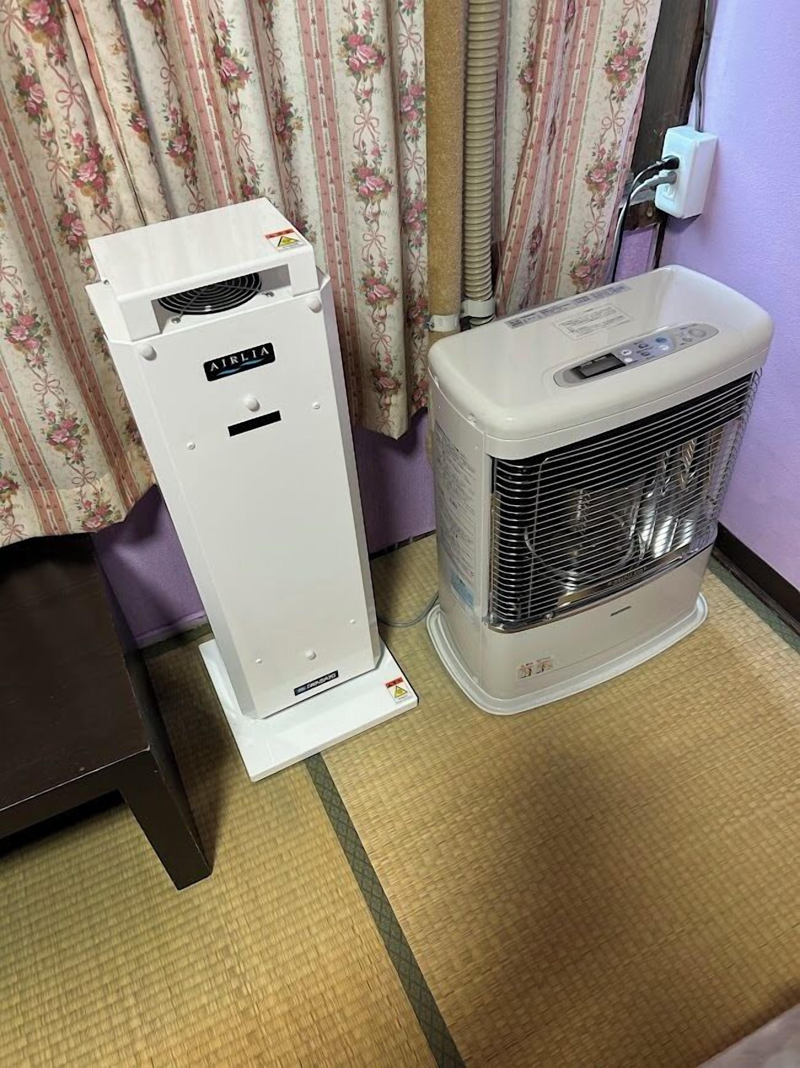 Two white air conditioning units in a room with floral curtains and a purple wall.